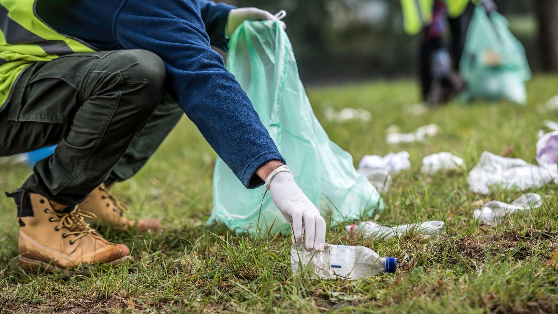 Volunteer in safety vest collecting plastic bottles during environmental cleanup